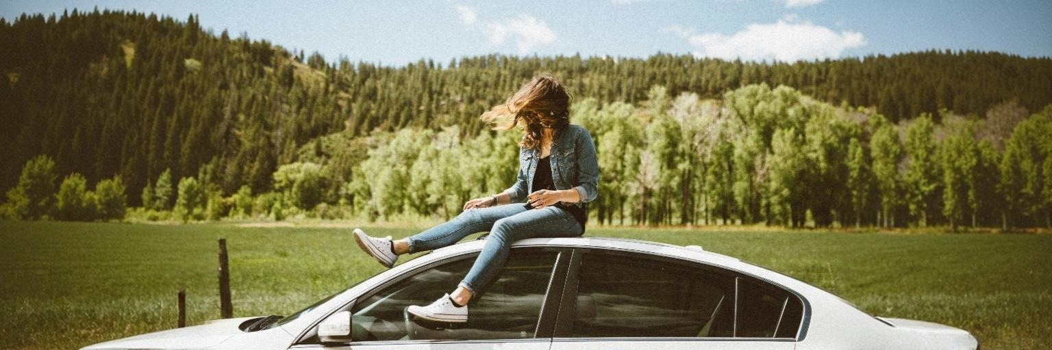 Young woman in denim sitting on car roof by averie woodard.